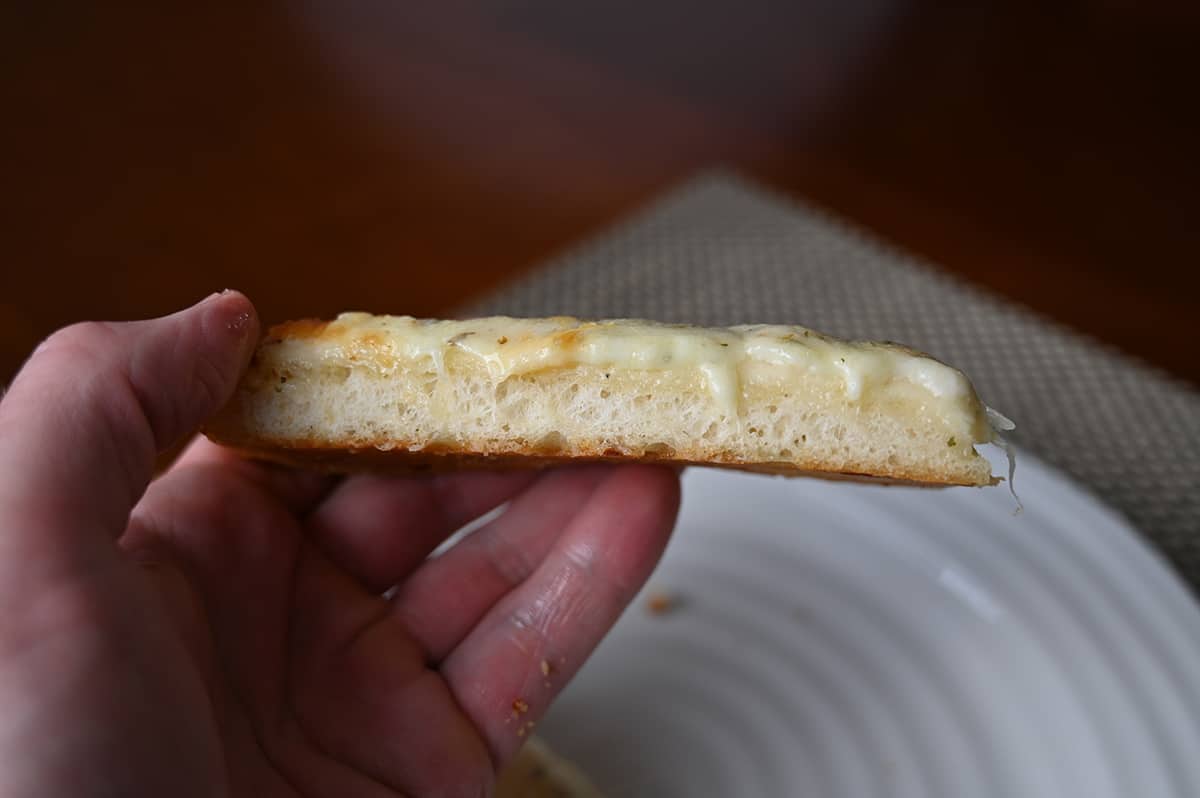 Closeup side view image of one slice of cheese bread being held close to the camera so you can see the depth of the crust.