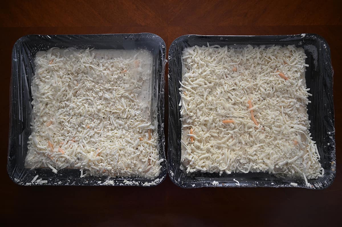 Image of two frozen cheese breads in a plastic tray with plastic wrap on top beside one another.