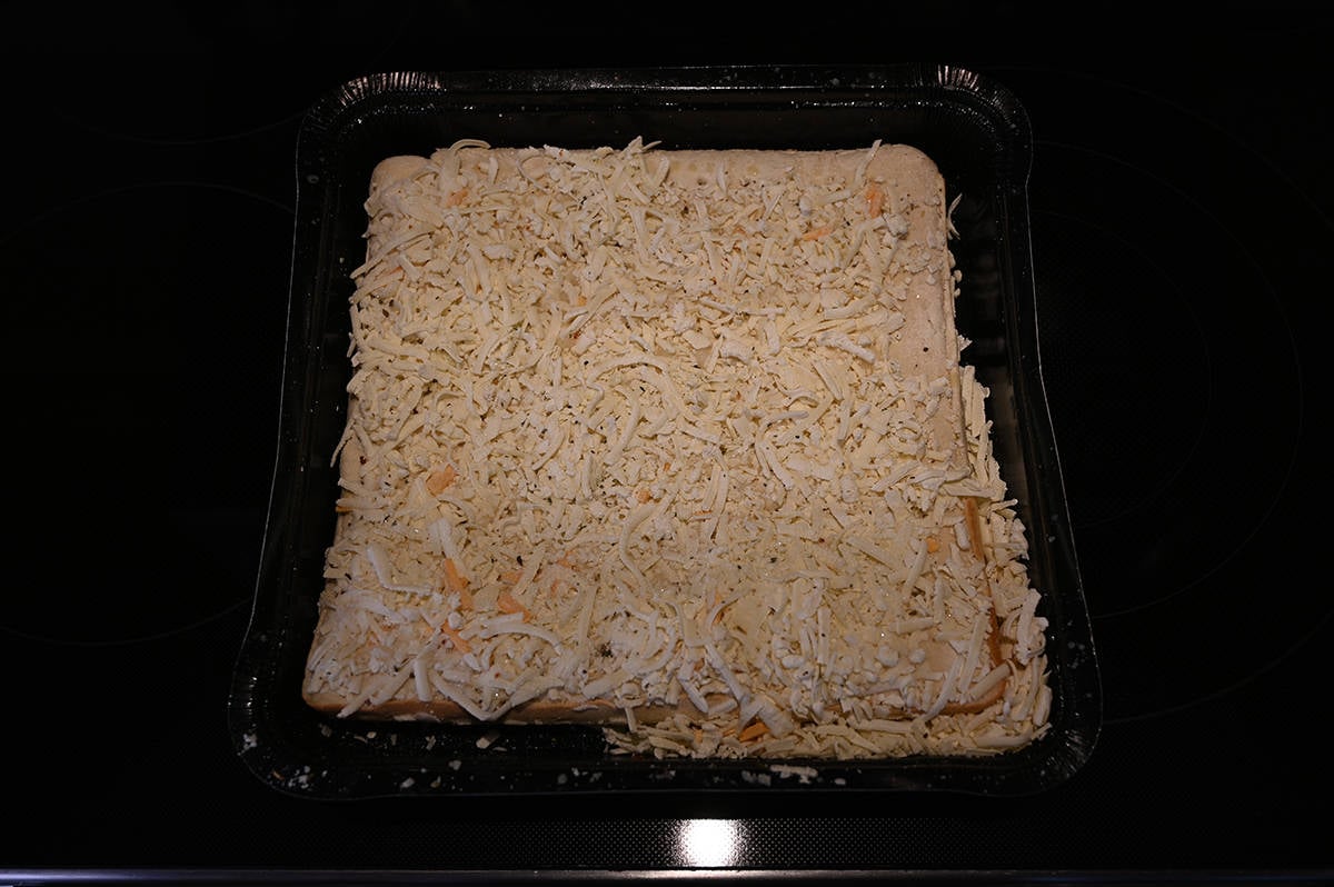 Closeup top down image of one frozen cheese bread with the plastic wrap off prior to baking it in the oven.