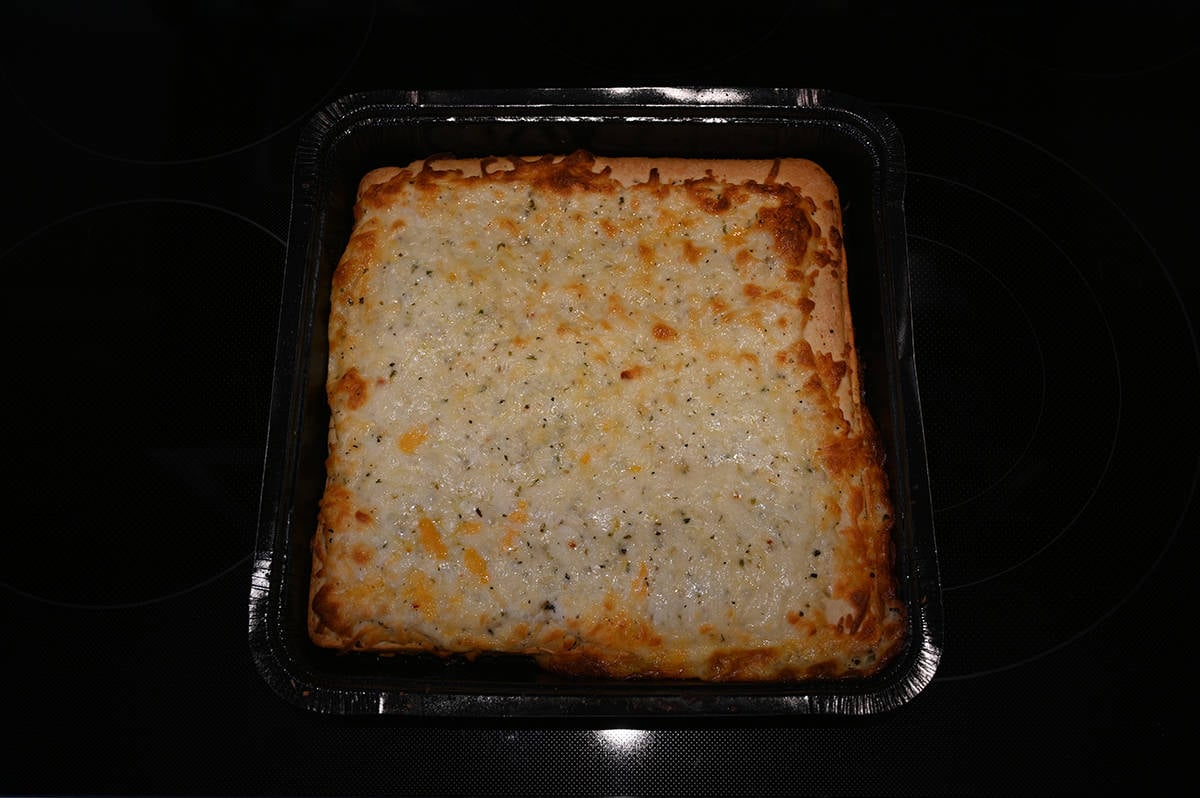 Closeup top down image of one fully baked cheese bread sitting on top of an oven in the tray it comes in.