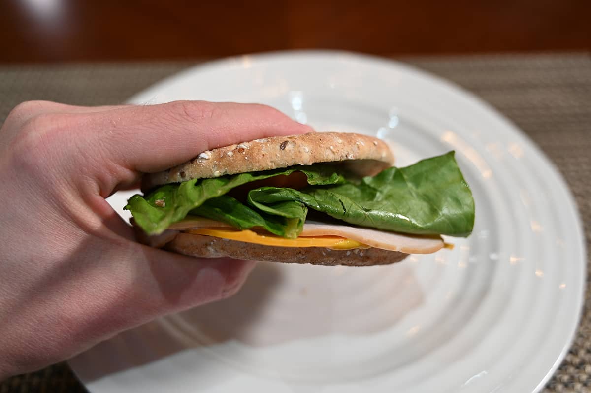 Closeup image of a hand holding one sandwich thin with turkey, lettuce and cheese in the middle. 