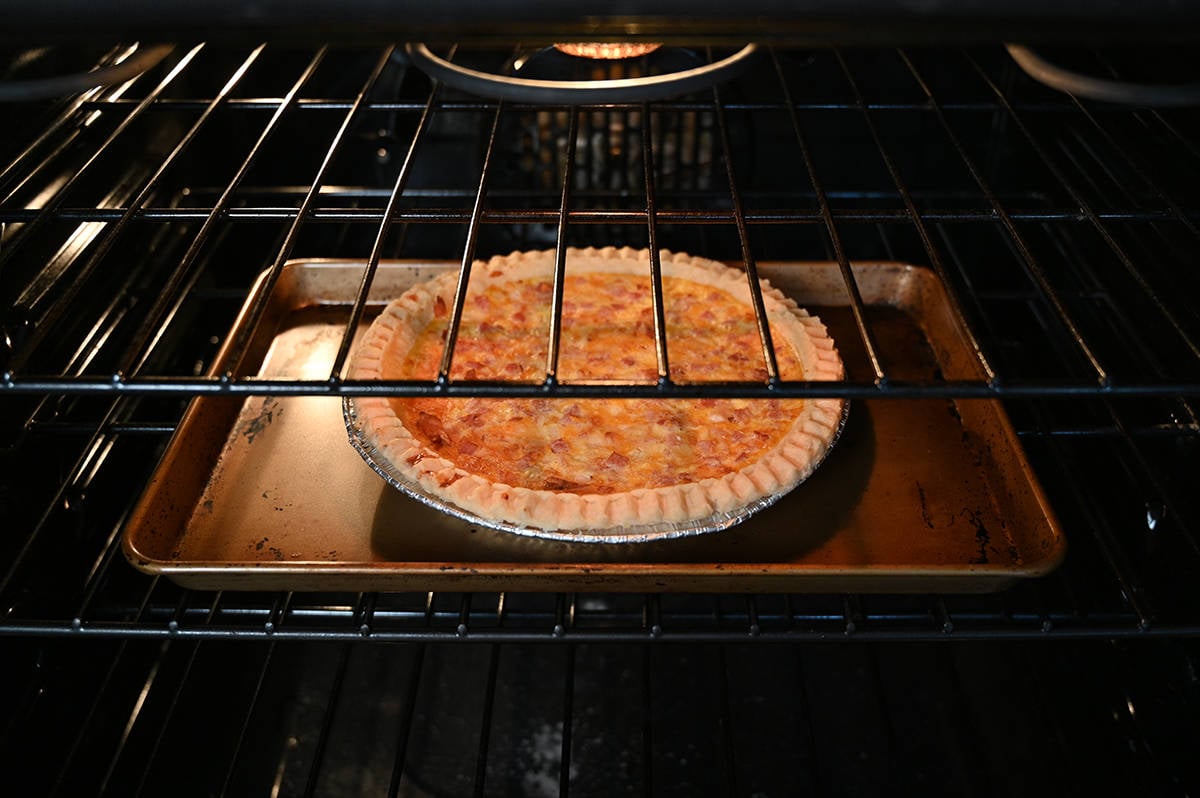 Side view image of a quiche on a cookie tray baking in an oven.