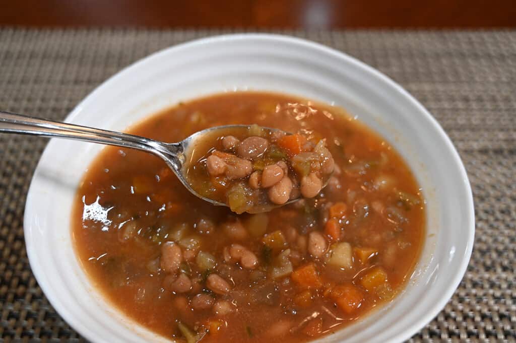 Side view image of a spoon scooping soup out of a bowl showing all the various ingredients in the bowl of soup.