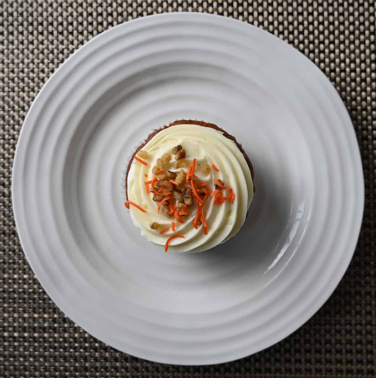 Top down image of one mini carrot cake served on a white plate, you can see orange shavings and walnuts on top of cream cheese icing.