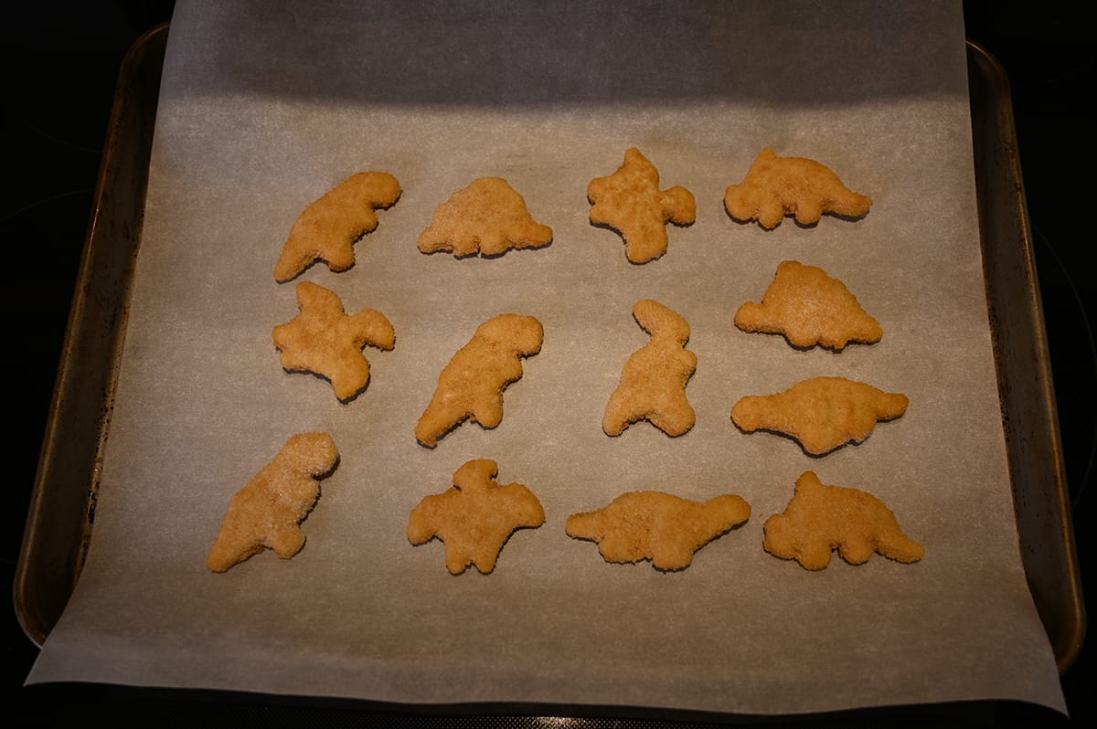 Top down image of a parchment paper lined baking tray with frozen dino nuggets on it.