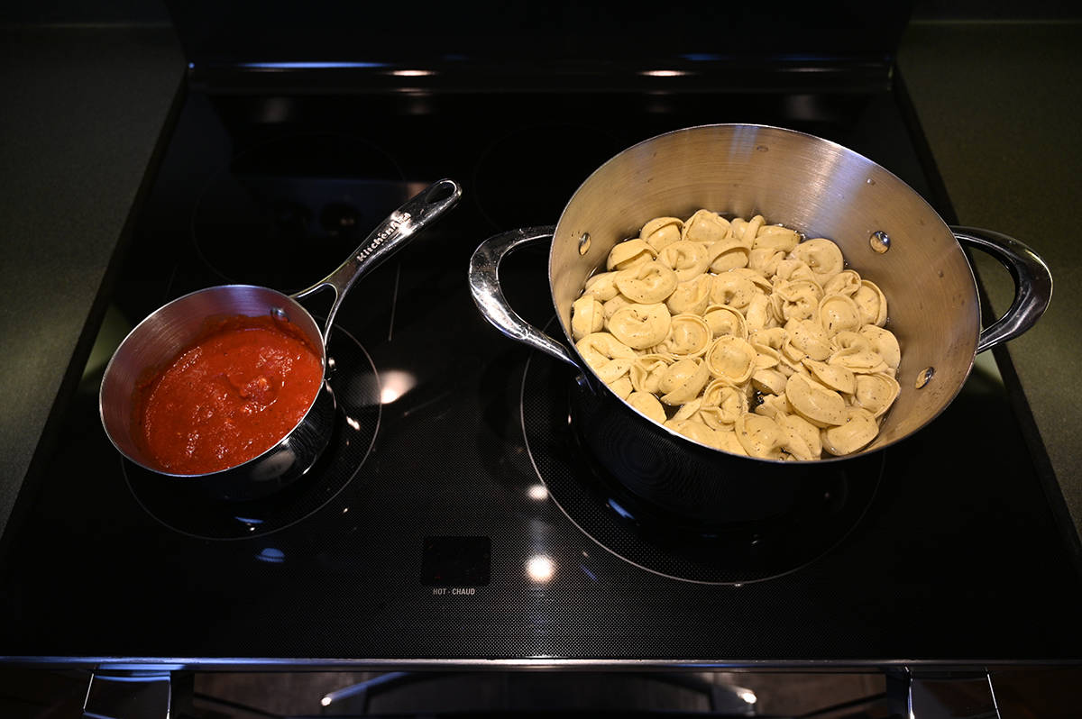 Image of a pot of tortelloni boiling on a stove beside a pot of red sauce.