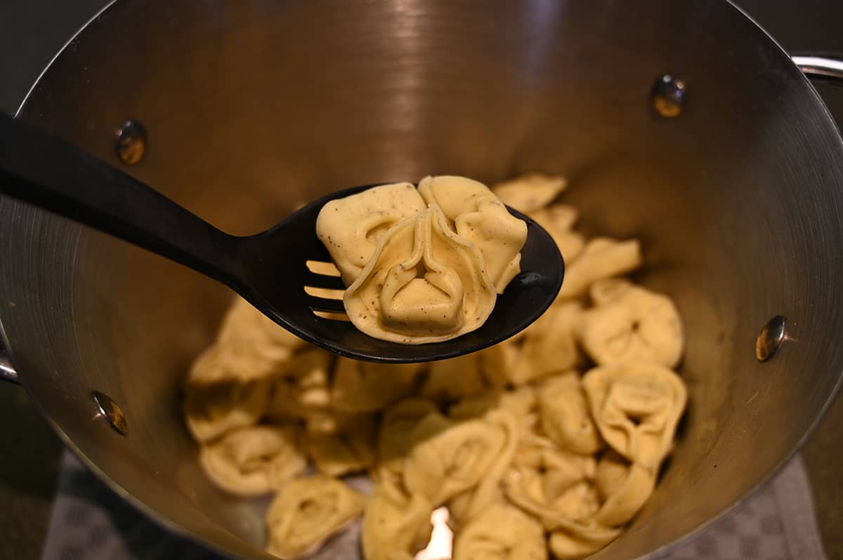 Closeup image of a spoon with tortelloni on it hovering over a pot of tortelloni.