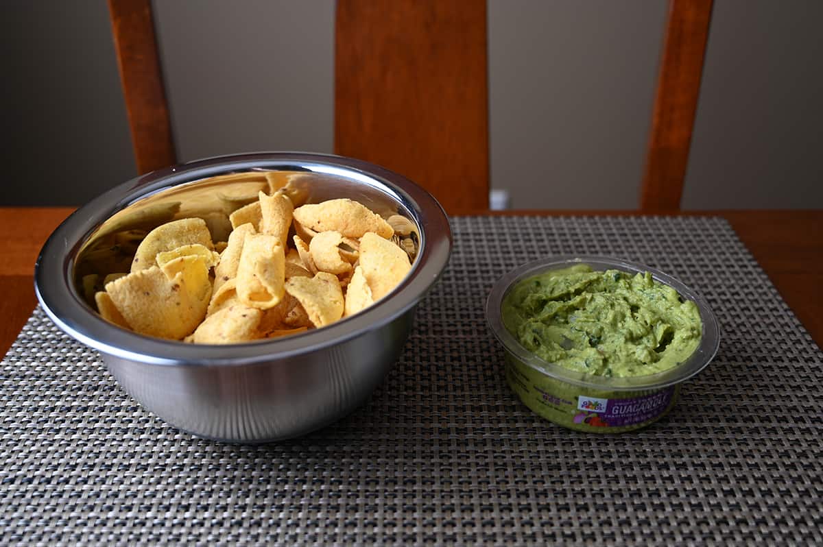 Side view image of a bowl of corn chips beside an open container of guacamole.