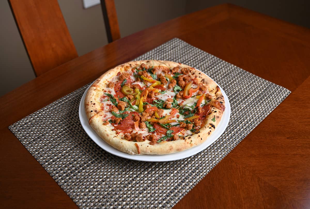 Image of a salami, sausage, arugula and  grilled peppers pizza baked and served on a white plate.