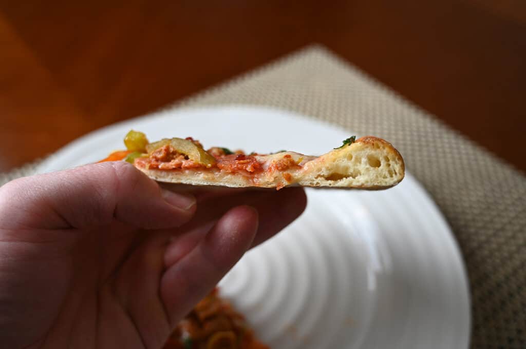 Side view image of a hand holding one slice of pizza close to the camera so you can see how thin the crust is.
