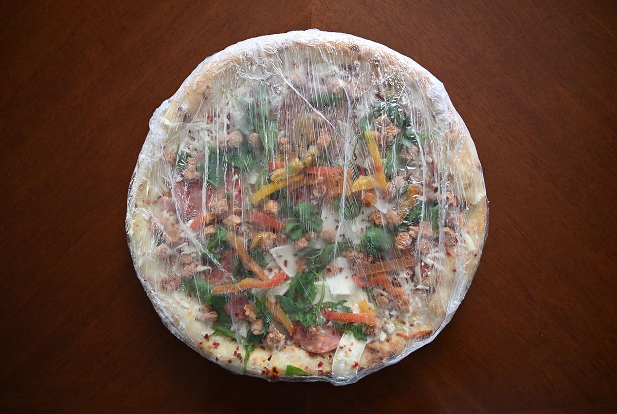 Image showing one frozen pizza wrapped in plastic, sitting on a table.