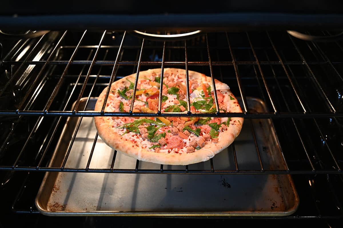 Image of a frozen pizza directly on an oven rack in the oven baking with a cookie sheet at the bottom of the oven to catch drippings.