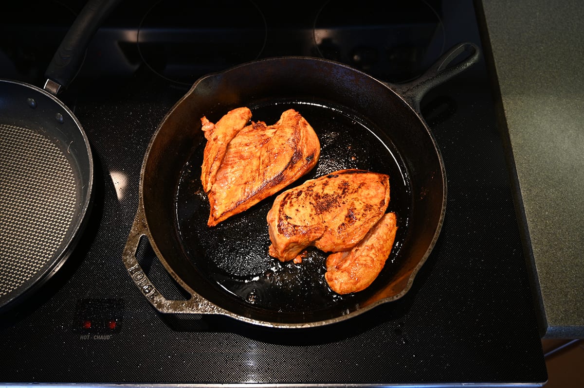Top down image of two sriracha seasoned chicken breasts cooking in a cast iron skillet.