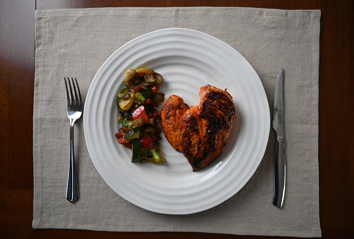 Top down image of a plate with a cooked chicken breast with sriracha seasoning on it beside vegetables.