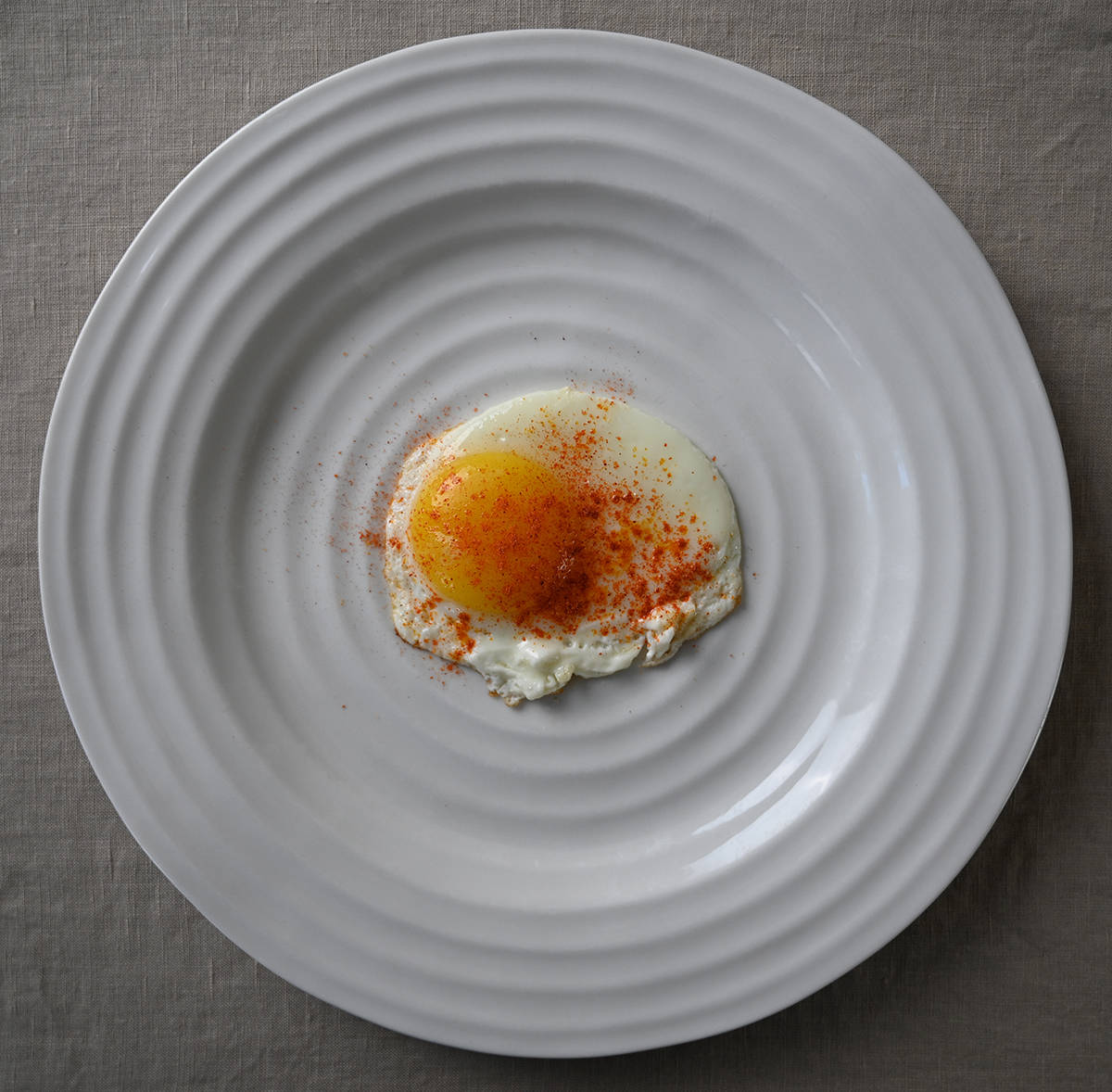 Top down image of a sunny side up egg with sriracha seasoning sprinkled on it.