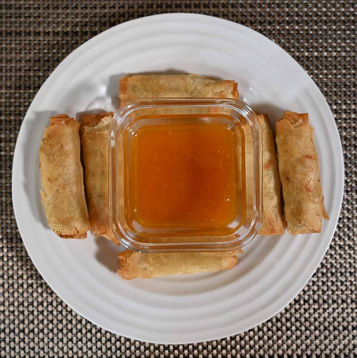 Top down image of a bowl of plum sauce in the center of a plate with six spring rolls surrounding it.