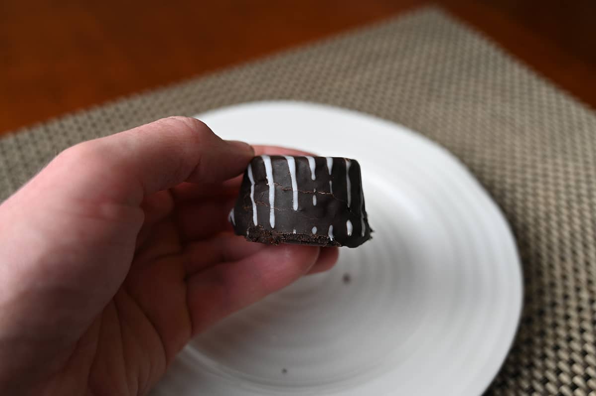 Closeup side view image of a hand holding one tuxedo cake bite close to the camera. 