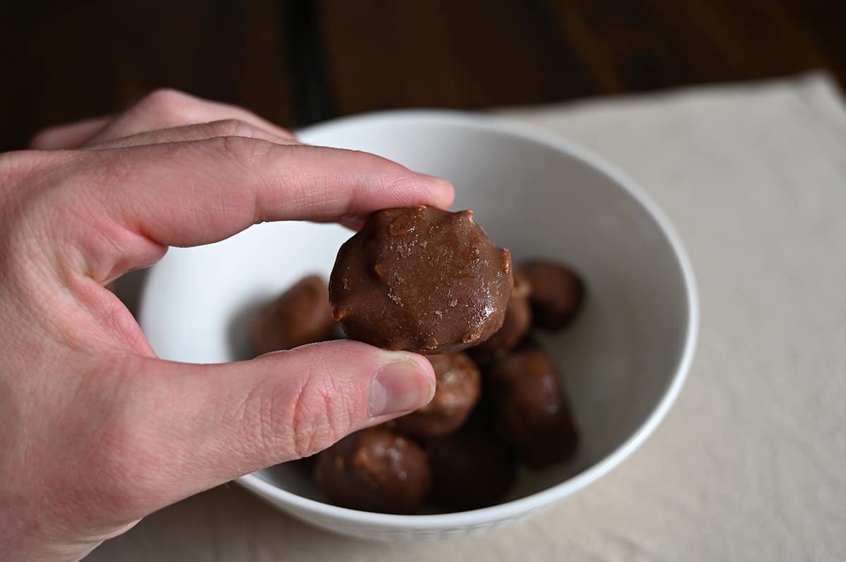 Closeup image of a hand holding one Reese's frozen banana slice close to the camera hovering over a bowl of frozen banana slices.