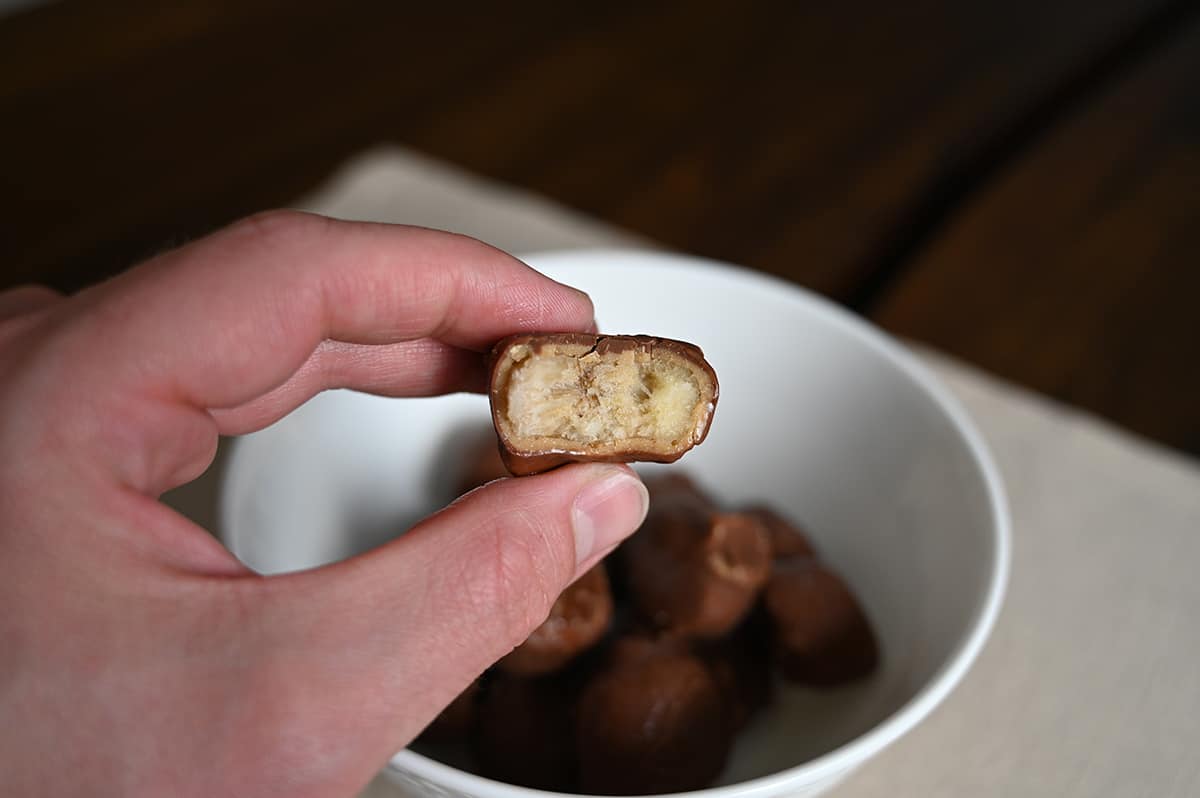 Closeup image of a hand holding one banana slice with a bite taken out of it so you can see the center.