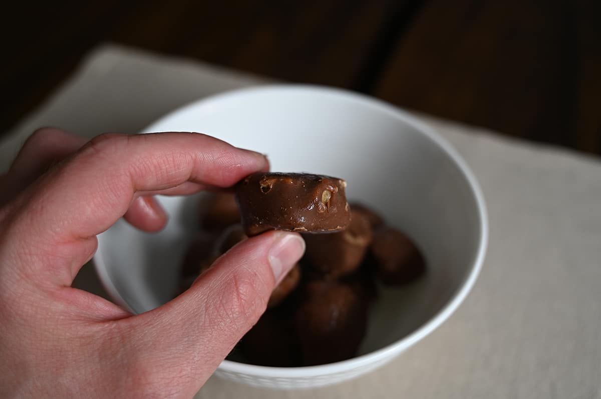 Sideview image of a hand holding one Reese's frozen banana slice over top a bowl. 