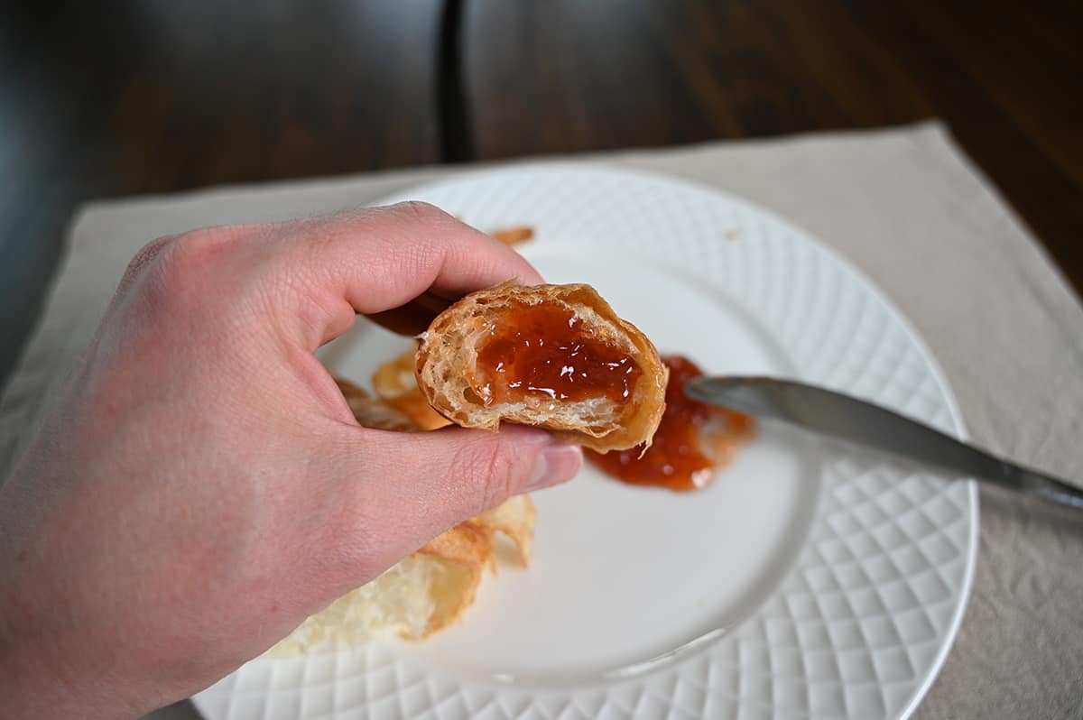 Closeup image of a hand holding one piece of croissant close to the camera with a dollop of jam on it.
