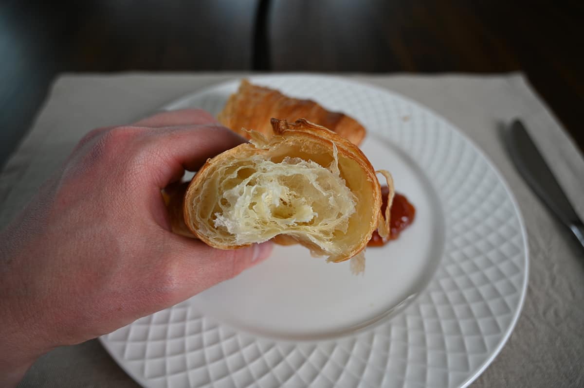 Closeup image of a hand holding one croissant with a few bites taken out of it so you can see the dough on the inside.