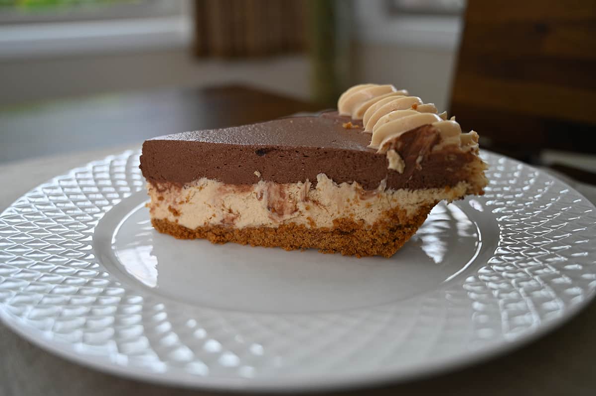Side view image of one slice of peanut butter pie on a white plate, served so you can see all the layers.