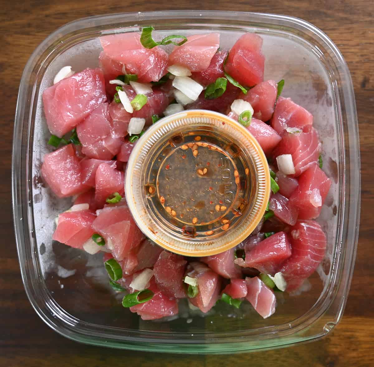 Top down image of an open container of the fresh shoyu poke. There's a container of sauce sitting on the top of the poke.