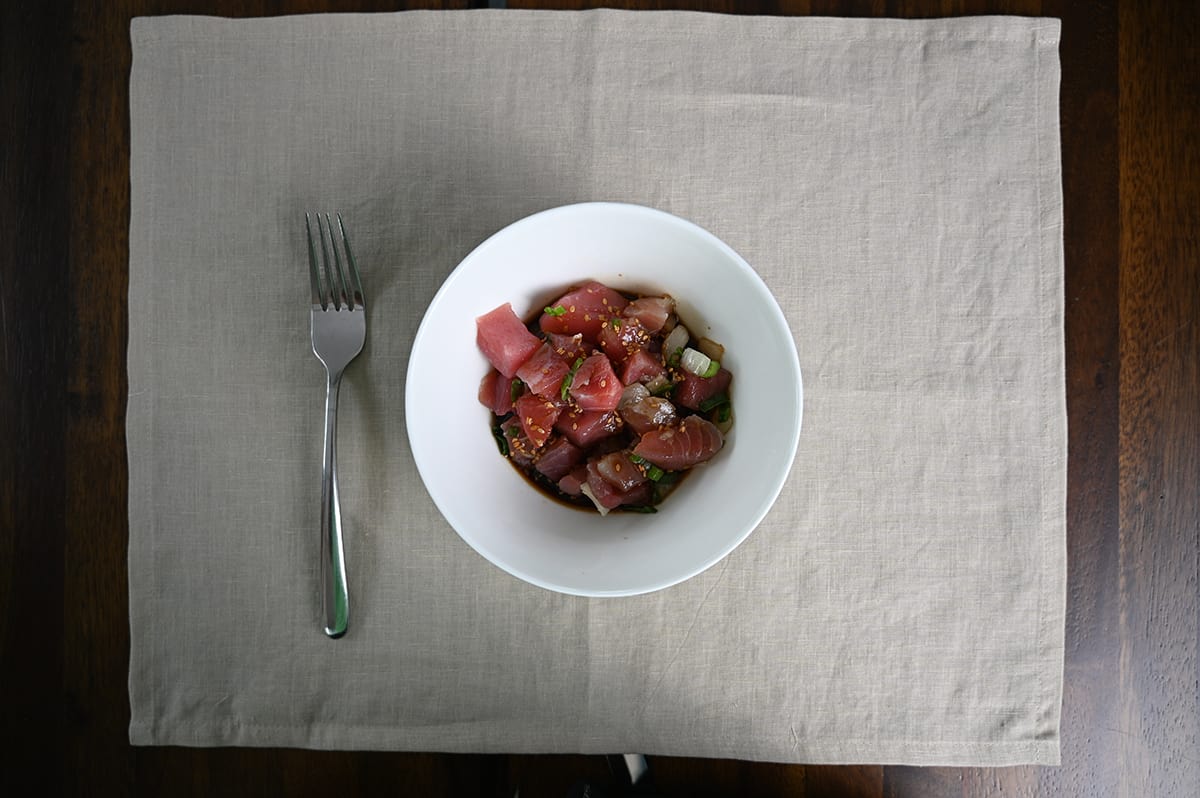 Top down image of a bowl full of fresh shoyu poke sitting on a table with a fork beside the bowl.