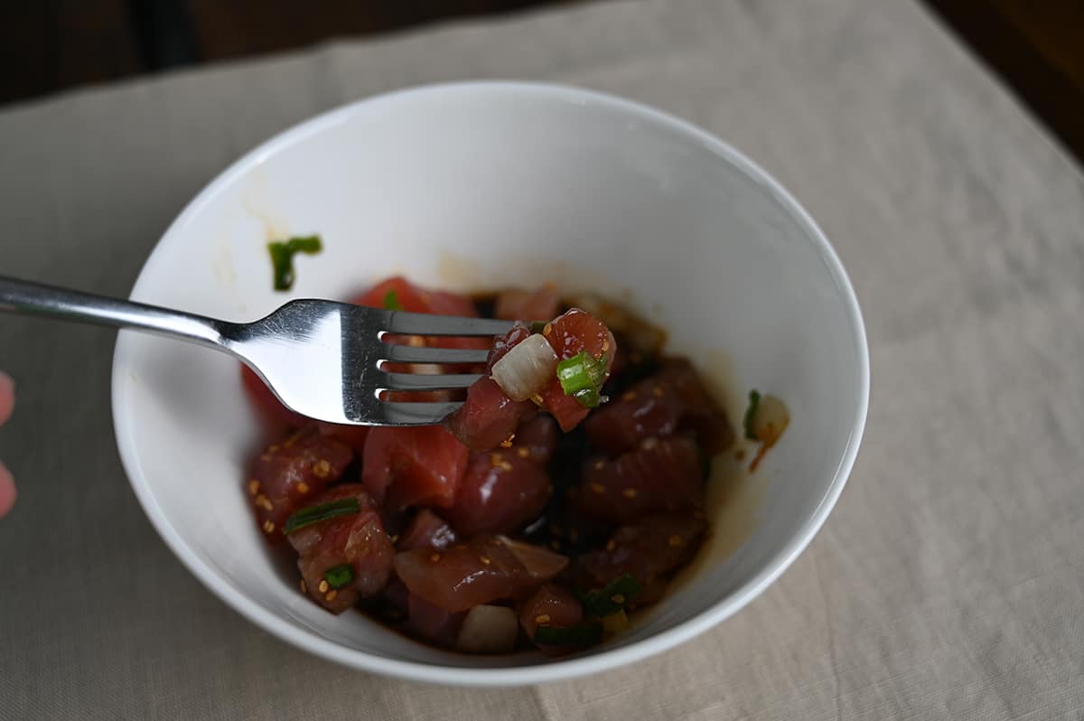 Closeup image of a fork hovering over a bowl of poke with a piece of fresh shoyu poke on the bowl.