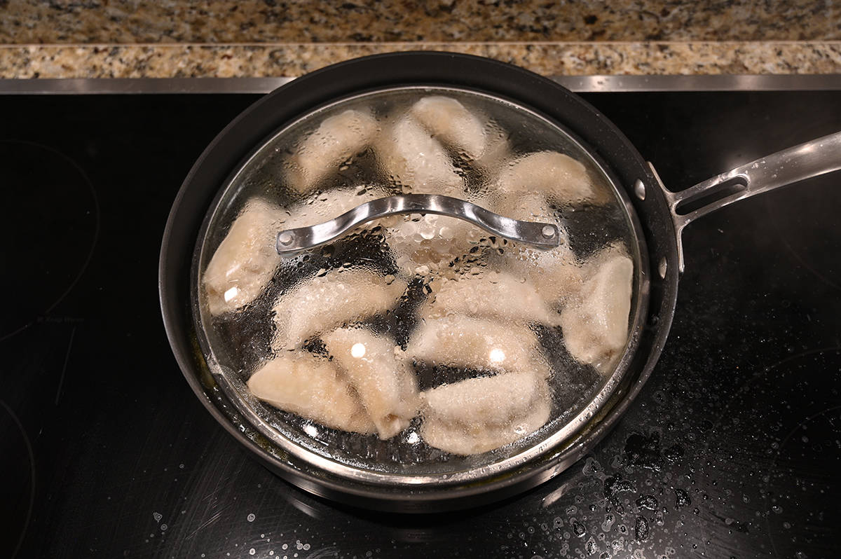 Top down image of the potstickers being steamed in a fry pan with the lid on.
