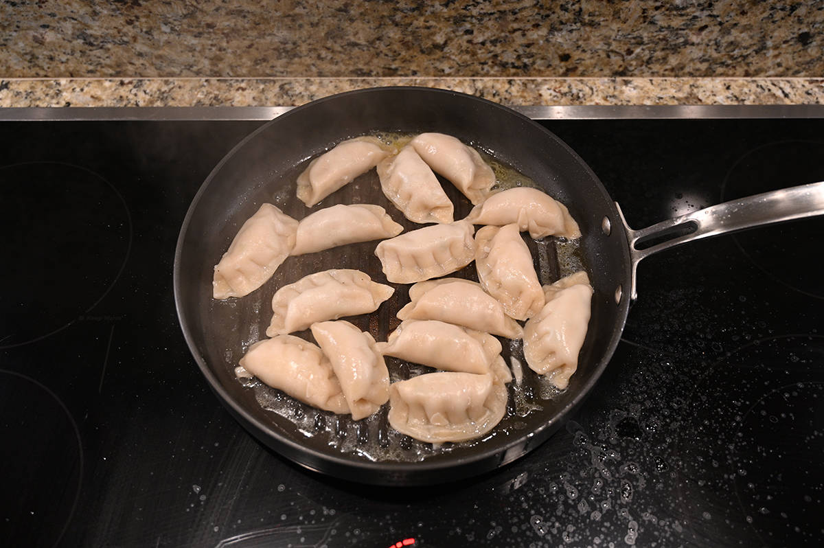 Top down image of a frying pan full of potstickers after being steamed. The lid is off and water is disappearing.