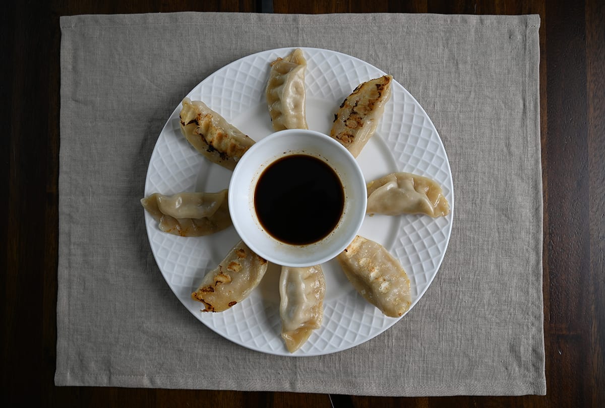 Image of a plate of potstickers served with a bowl of dipping sauce in the middle.