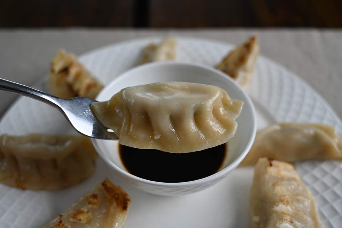 Image of a fork holding one potsticker on it hovering over a bowl of sauce.