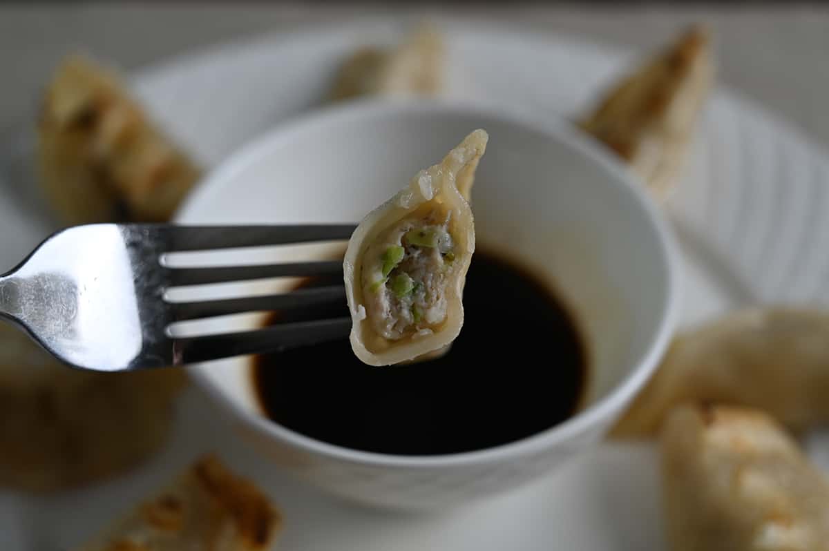 Image of one piece of potsticker on a fork being dipped in sauce, close to the camera so you can see the filling.