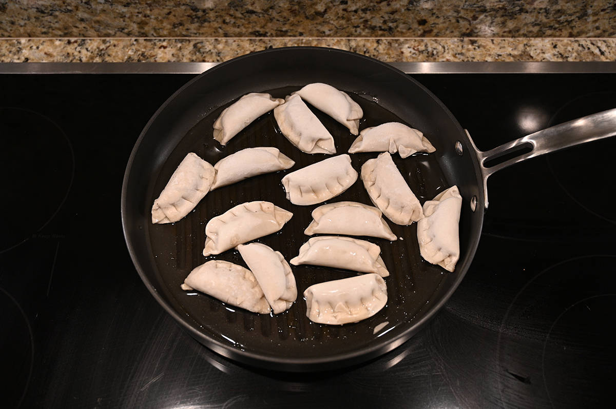 Top down image of frozen potstickers being put in the fry pan with oil.