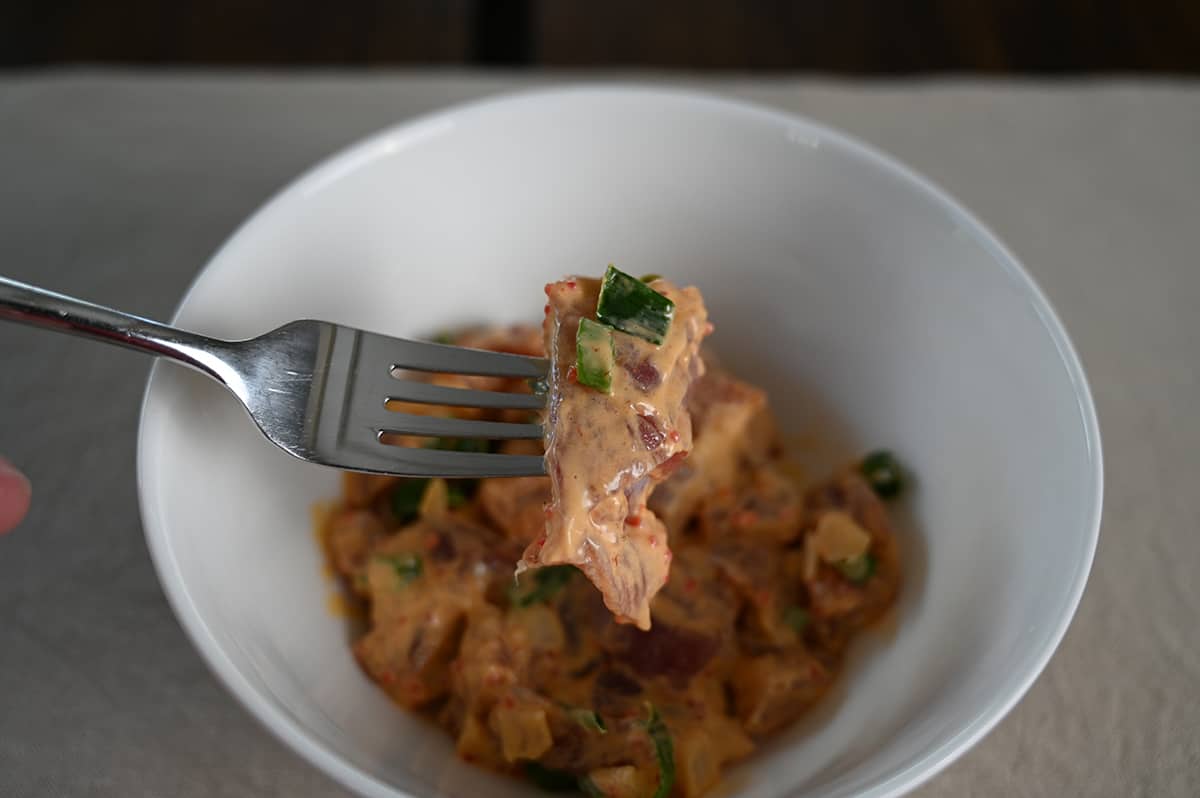 Image of a fork hovering over a bowl of Spicy Ahi Poke, the fork has a piece of poke on it.