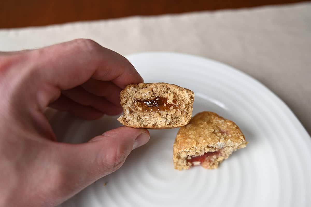 Closeup image of a hand holding one apple stuff'd oat bite close to the camera cut in half so you can see the apple filling.