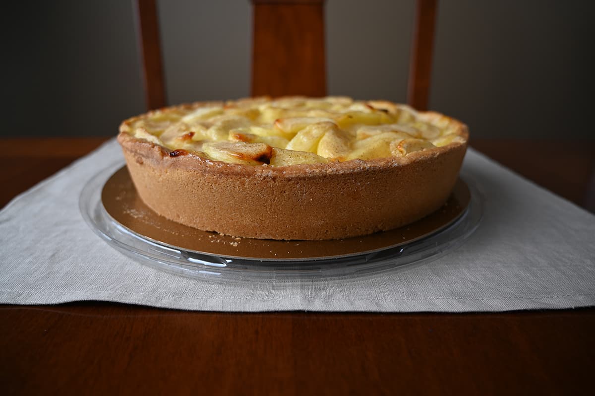 Side view image of the whole apple cake, out of the package sitting on a table. You can see the cake crust on the outside and how tall and deep the cake is. 