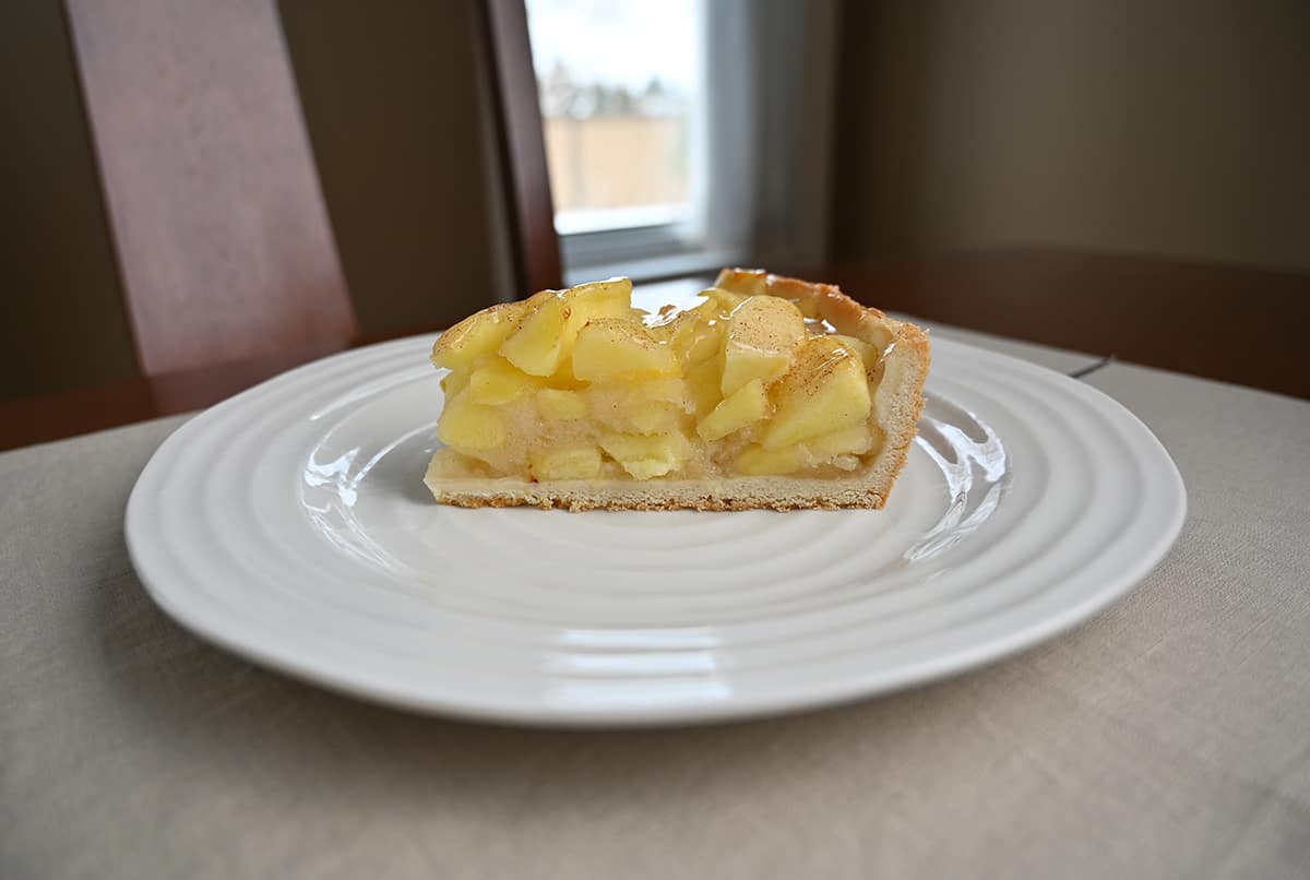 Side view image of one piece of apple cake served on a white plate showing the cake is very tall and loaded with apples in the middle.