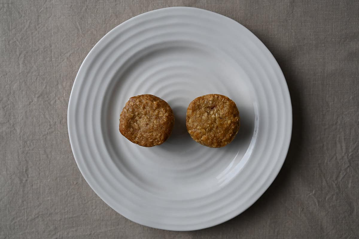 Top down image of two oat bites sitting on a white plate, apple on the left, strawberry on the right.