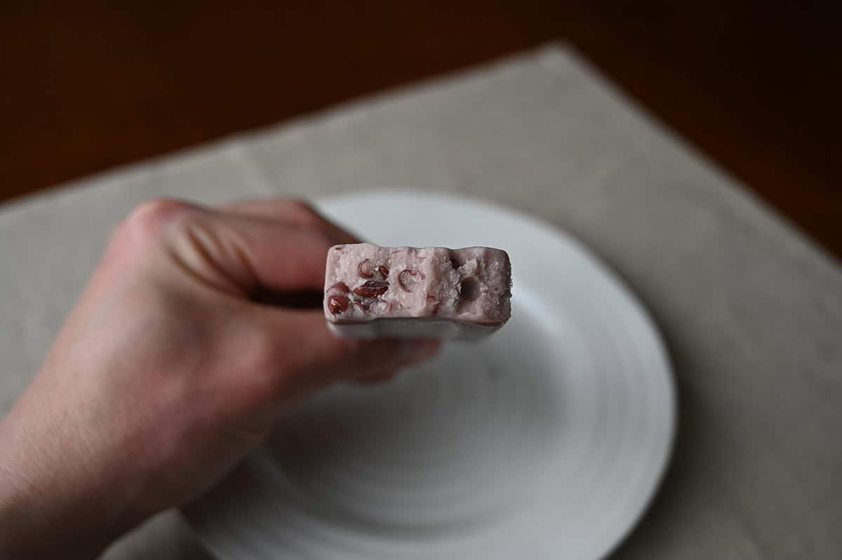 Image of a hand holding a frozen dessert bar with a few bites taken out of it so you can see the red beans in the bar.