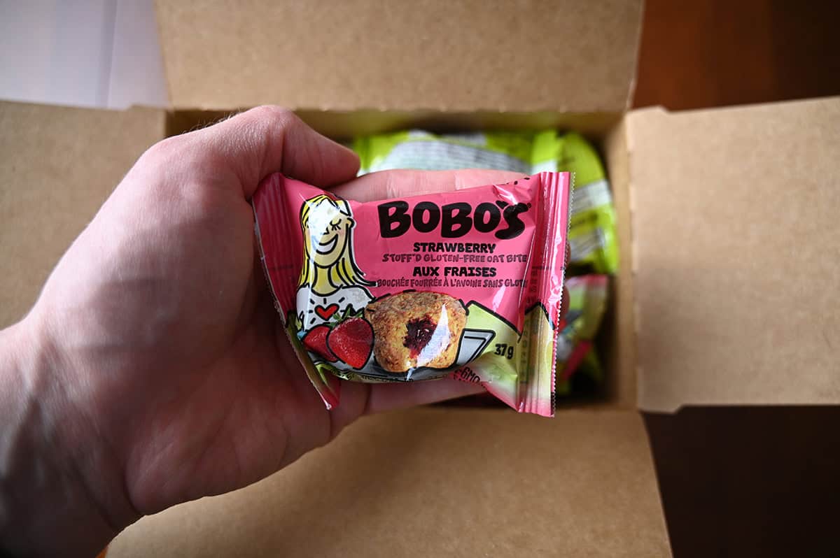 Closeup image of a hand holding one packaged strawberry oat bite close to the camera.