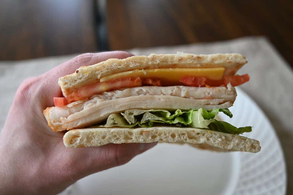 Sideview closeup image of a hand holding one sandwich close to the camera so you can see all the fillings in the sandwich.
