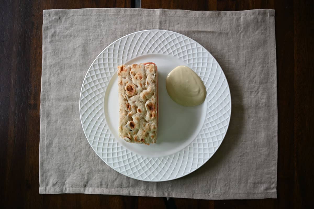 Top down image of a sandwich served beside a bit of dipping sauce on a white plate.