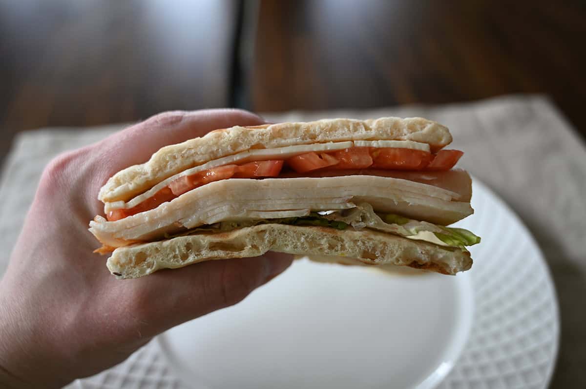 Sideview closeup image of a hand holding one sandwich close to the camera so you can see all the fillings in the sandwich.