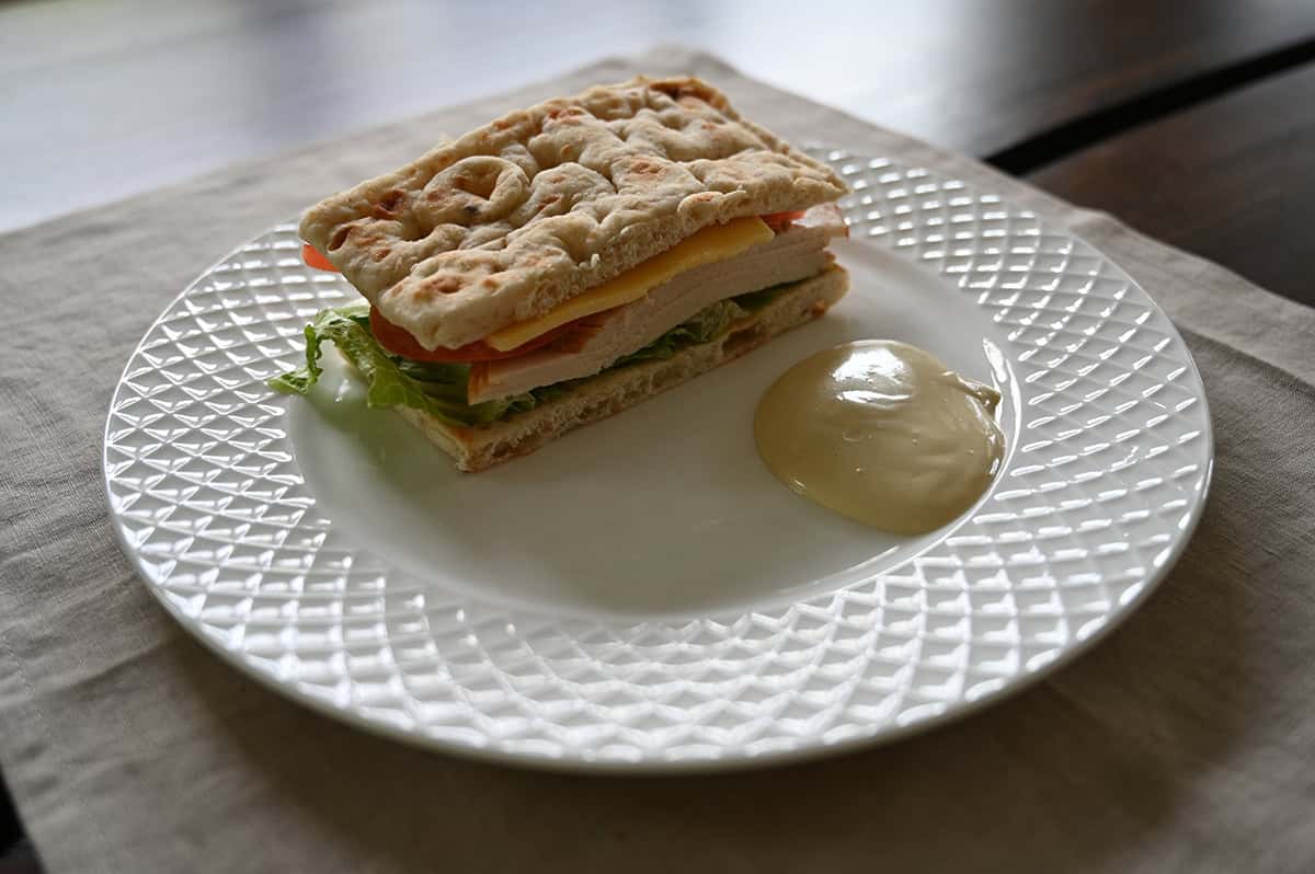 Sideview top down image of one sandwich served on a white plate. Beside the sandwich is a bit of dipping sauce.