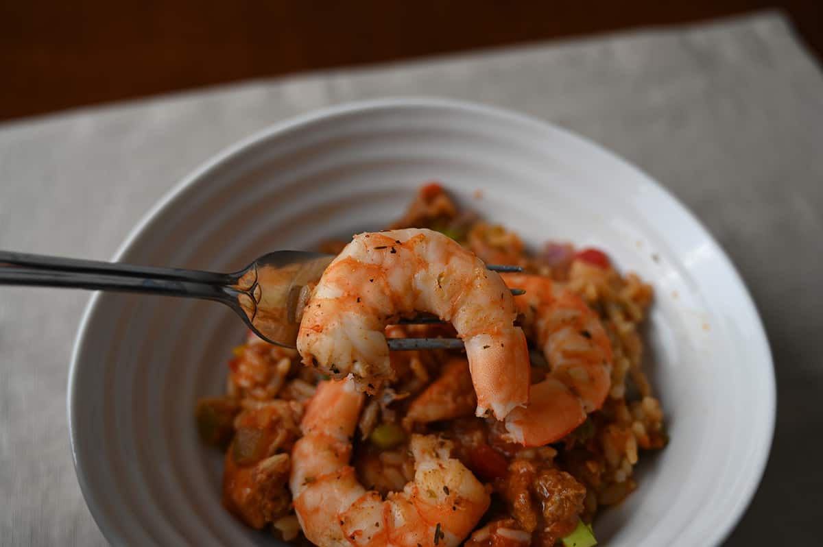 Closeup image of a fork with a shrimp on it hovering over a bowl of jambalaya.