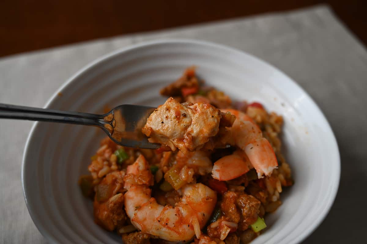 Closeup image of a fork with a piece of chicken on it hovering over a bowl of jambalaya.