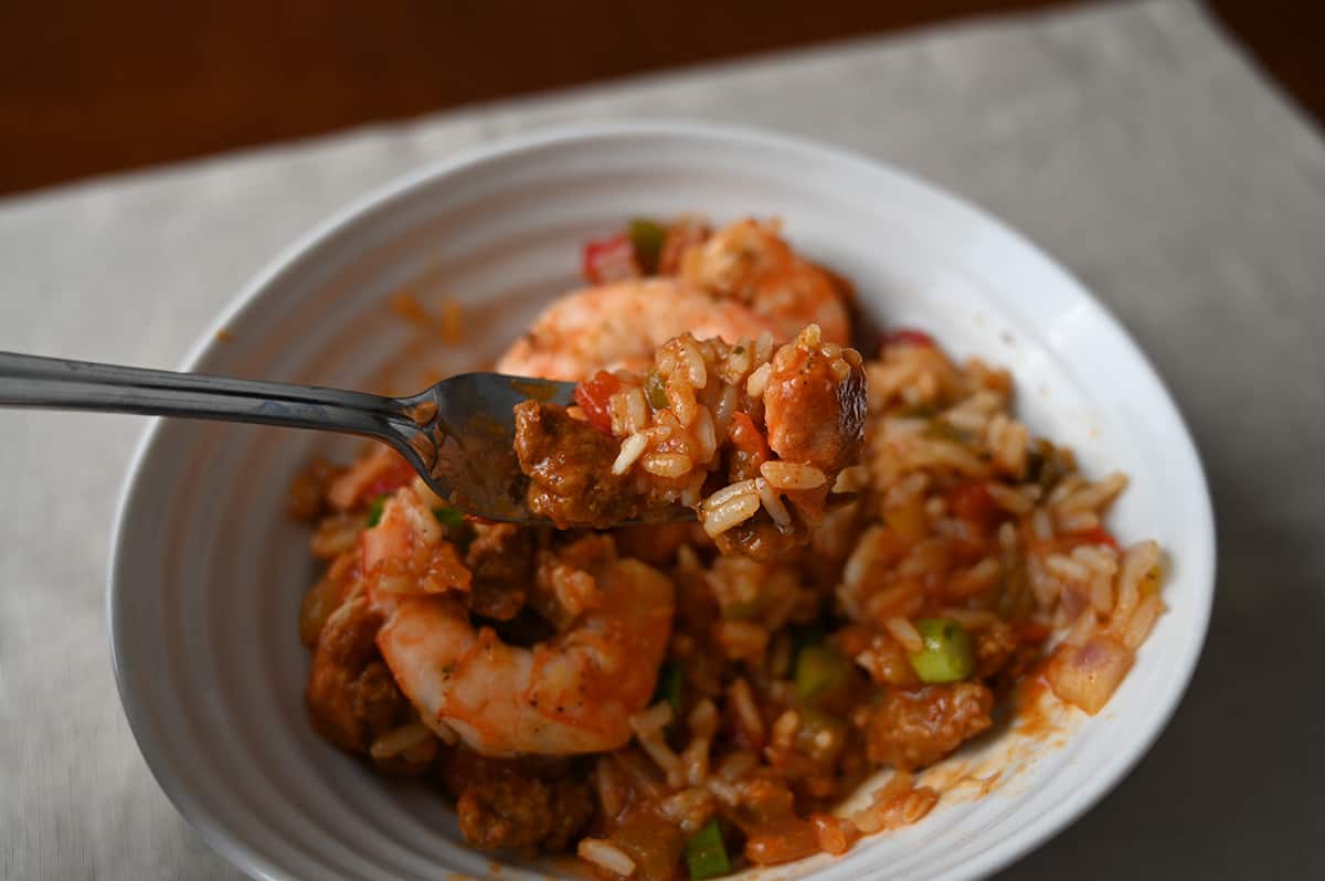 Closeup image of a fork with sausage and rice on it hovering over a bowl of jambalaya.